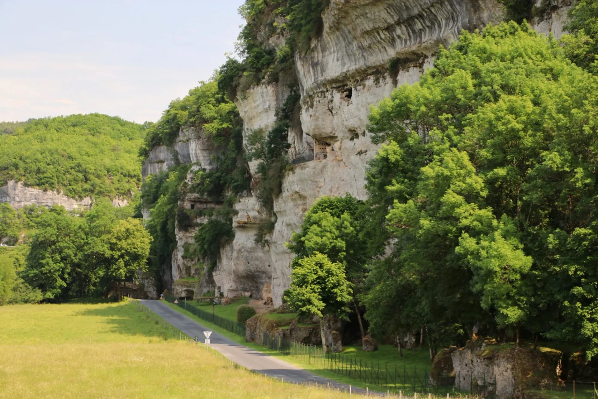 Road winding past tall limestone cliffs covered in green trees near La Roque