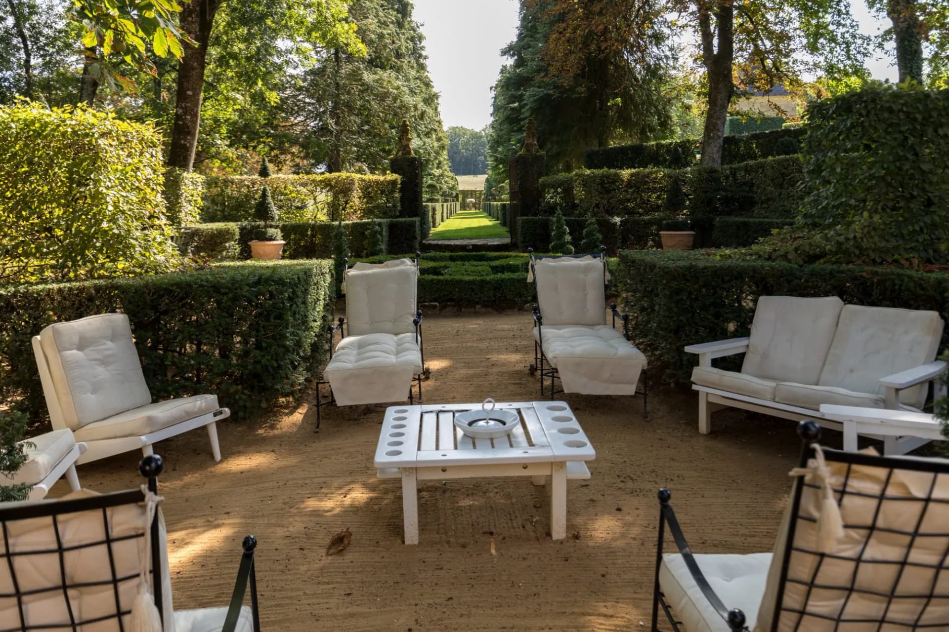Outdoor seating area with white cushions in a formal garden with manicured hedges