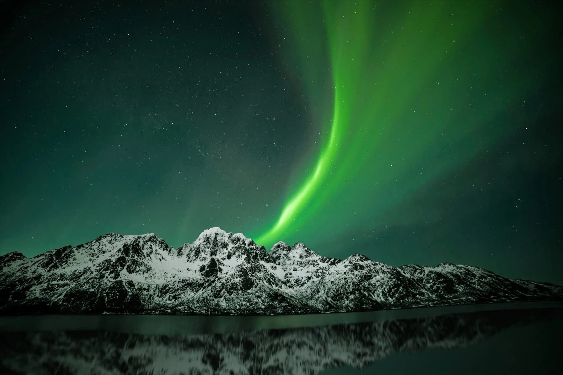 Aurora Borealis over snow-covered mountains reflected in dark water at night, Svolvær.