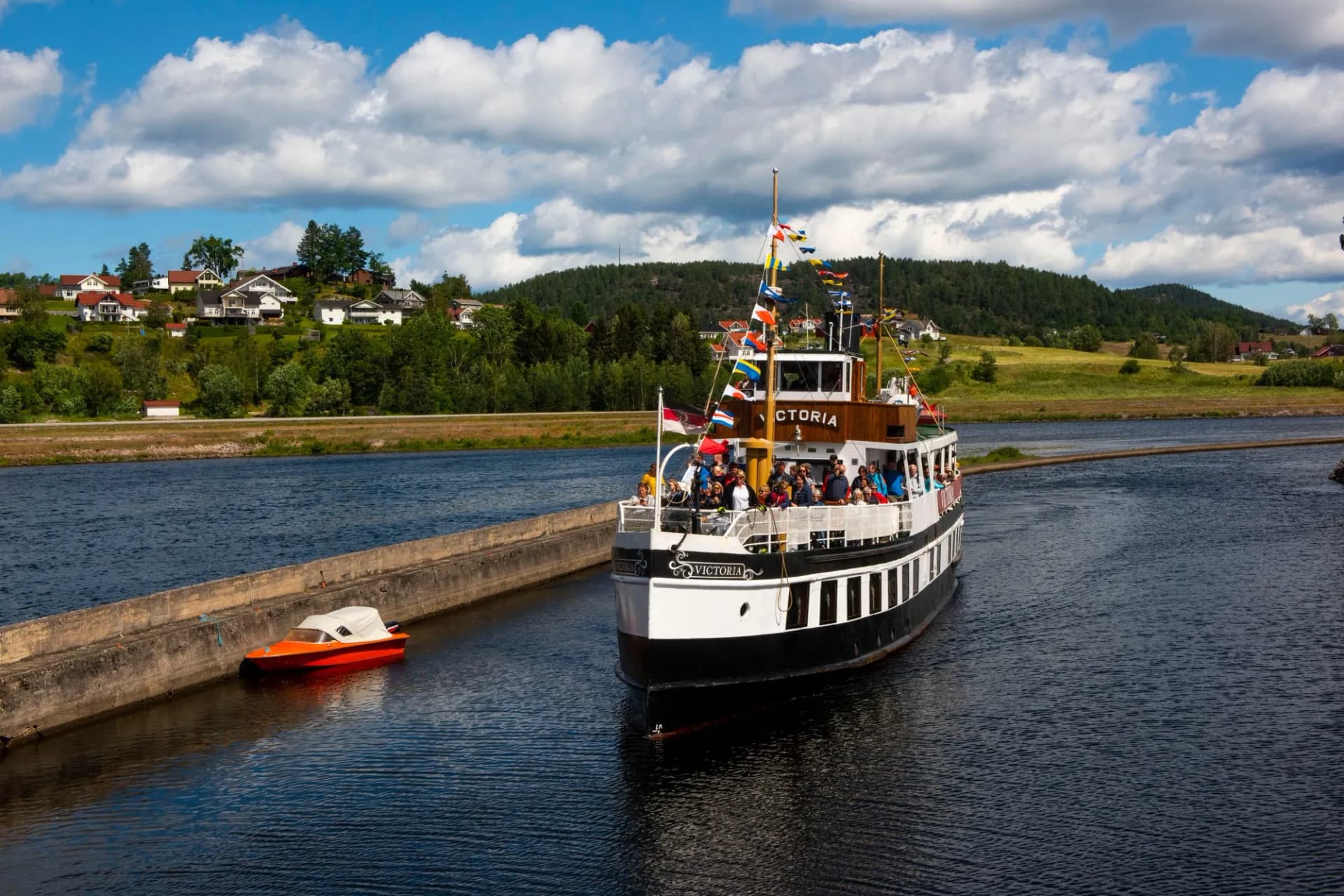 Passenger boat Victoria navigating canal waters past a small orange boat near a concrete lock wall.