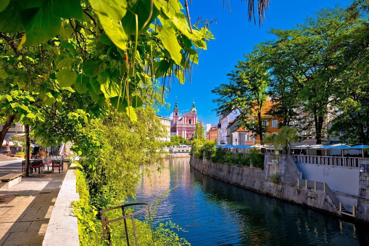 River flowing through Ljubljana with Franciscan Church and lush spring foliage.