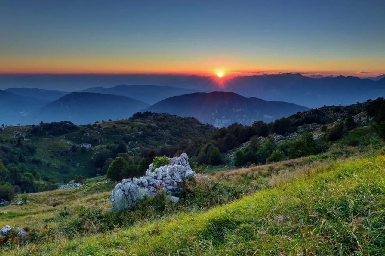Mountain landscape at sunset with rolling grassy hills and layered blue peaks in the distance.