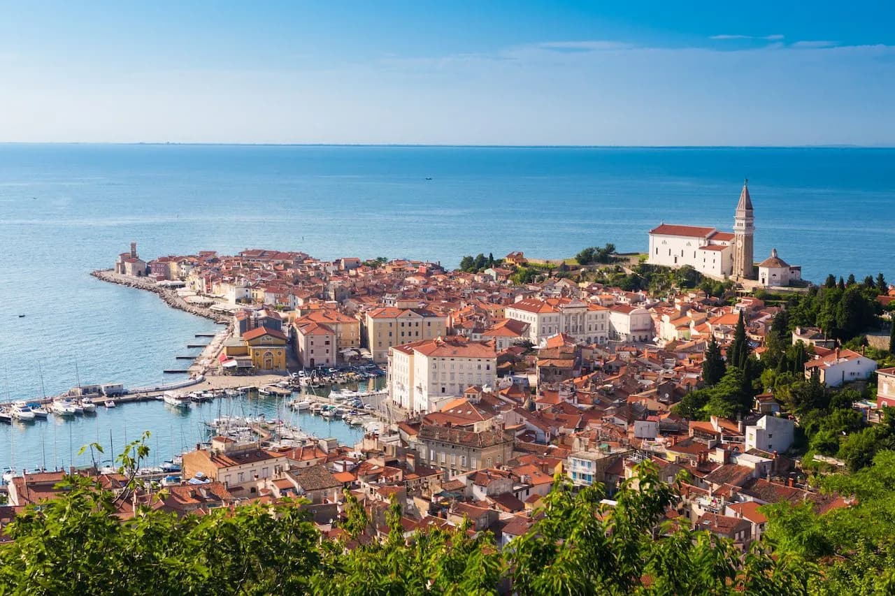 Coastal town with red roofs, harbor, and church tower overlooking the bright blue sea.