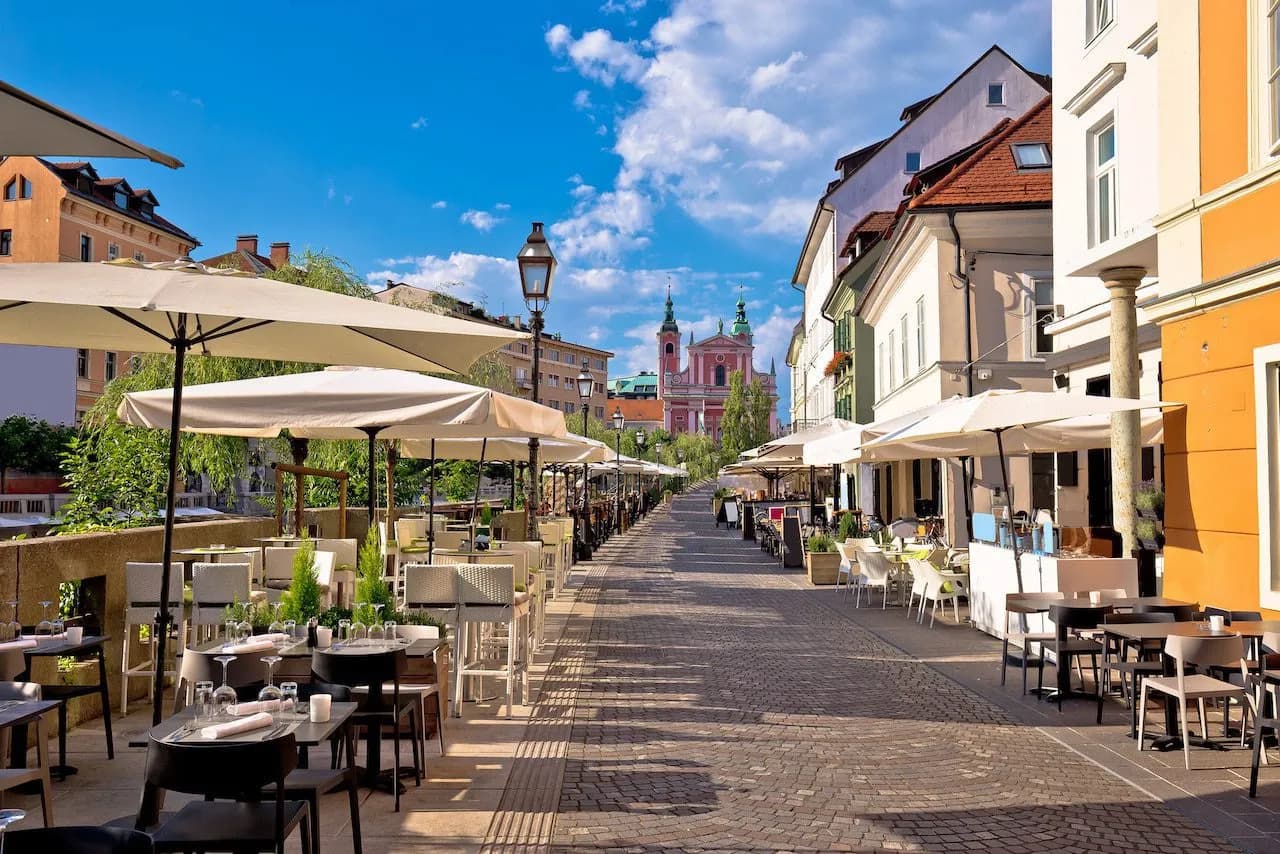 Outdoor cafe dining on cobblestone street toward pink church in Ljubljana Center.
