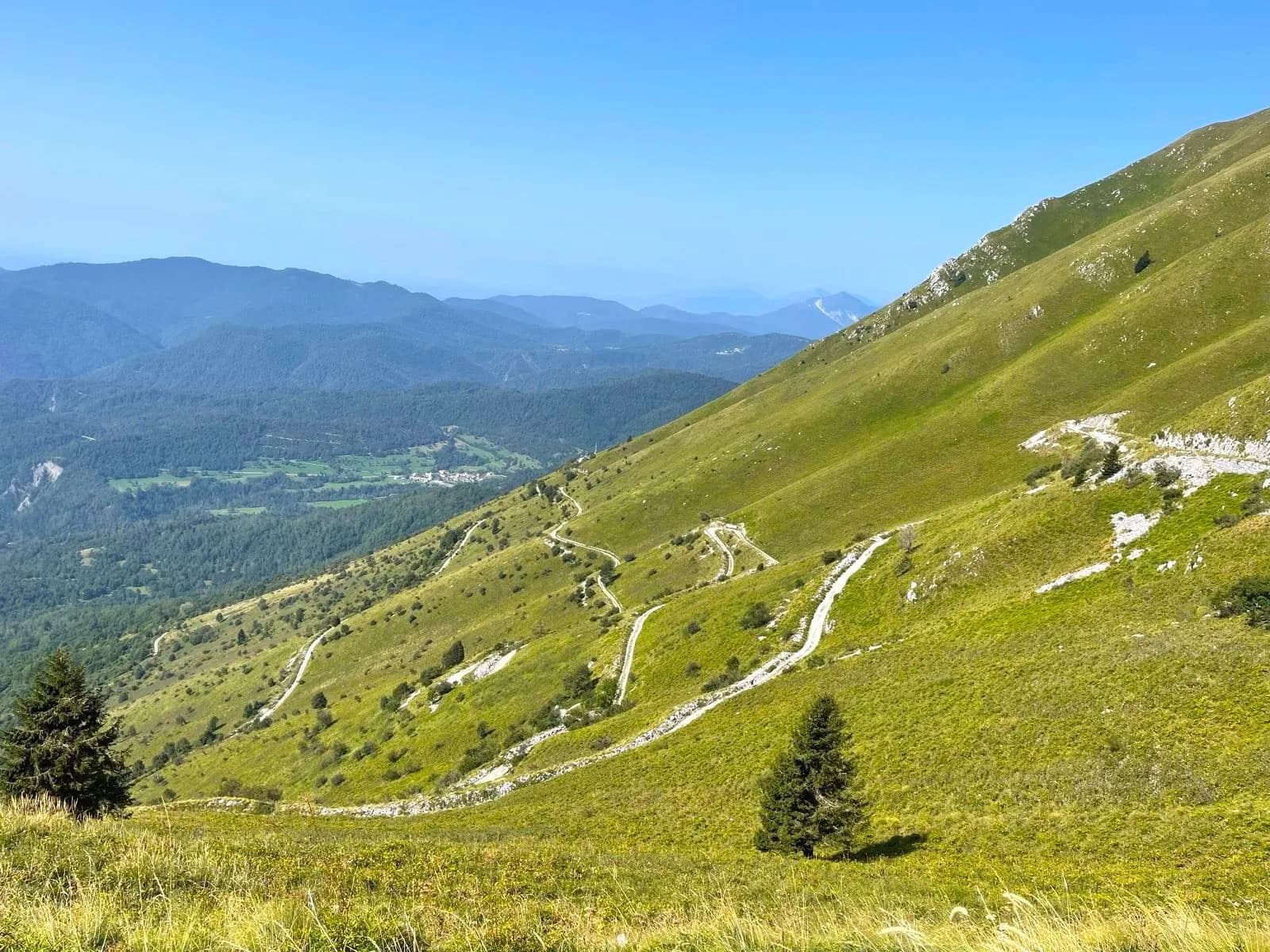 Winding dirt road ascending steep grassy mountain slope with distant forested valleys