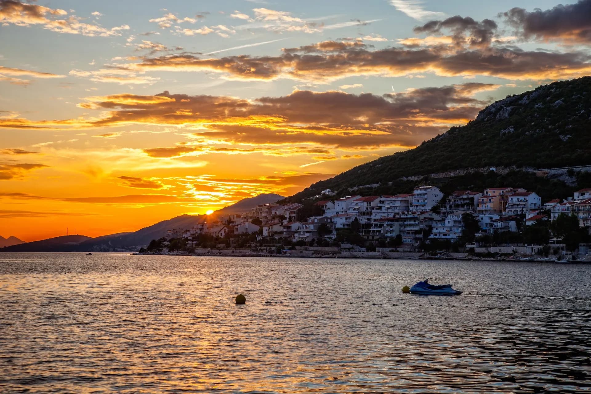 Jet ski on water near coastal town with houses climbing a hill at sunset