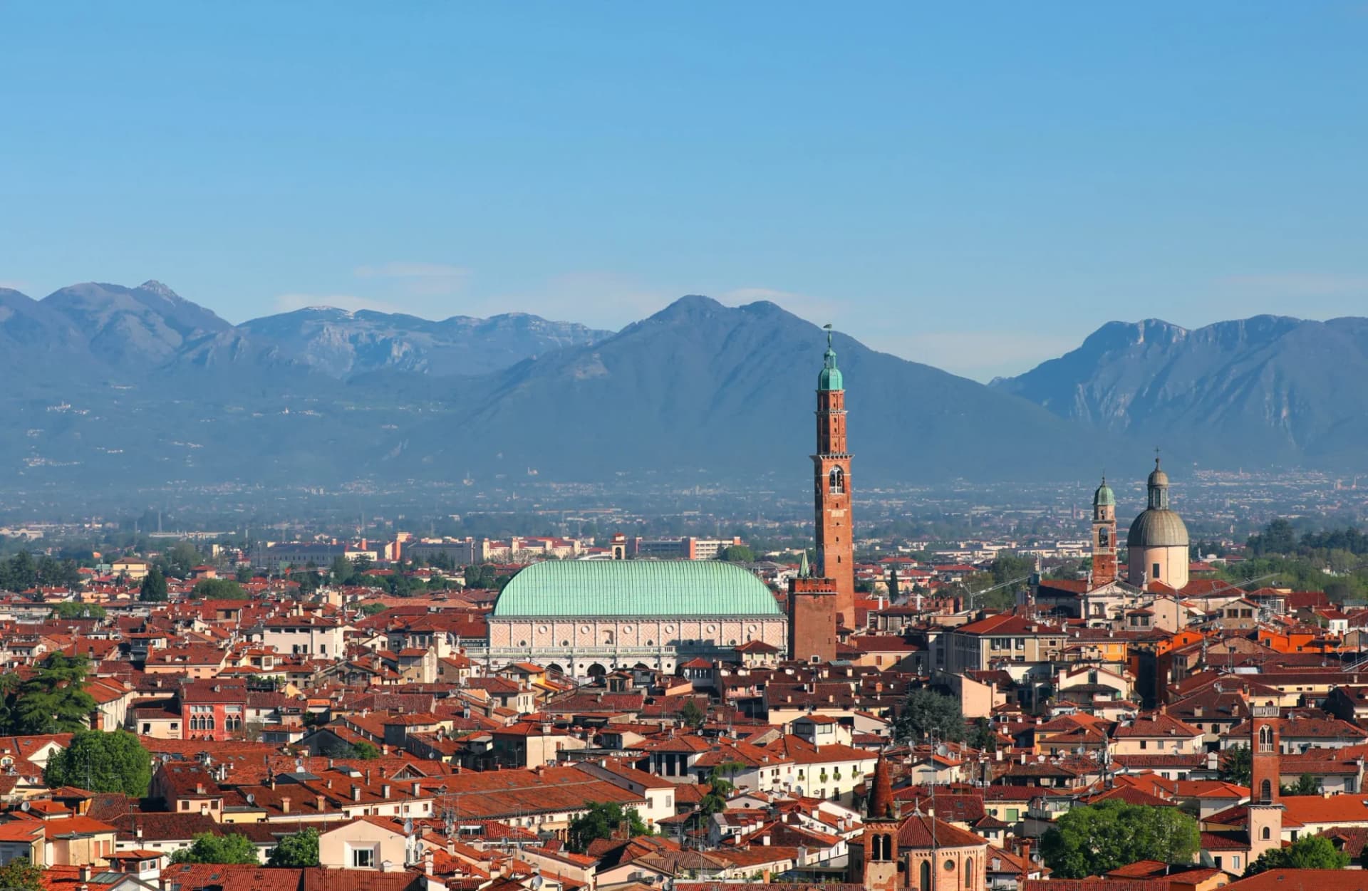 Vicenza skyline with Basilica Palladiana and mountains in the background under clear blue sky.