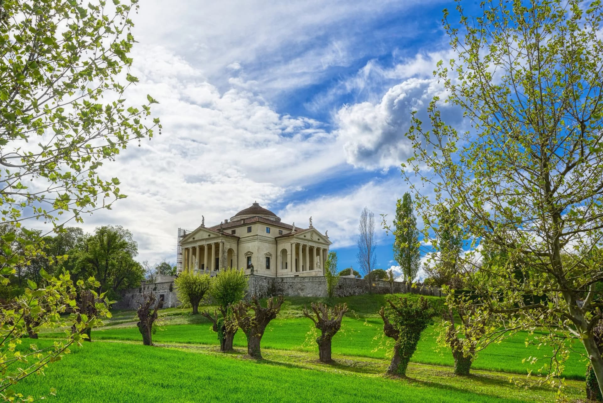 Villa La Rotonda with classical columns, green lawn, and trees under a blue sky.