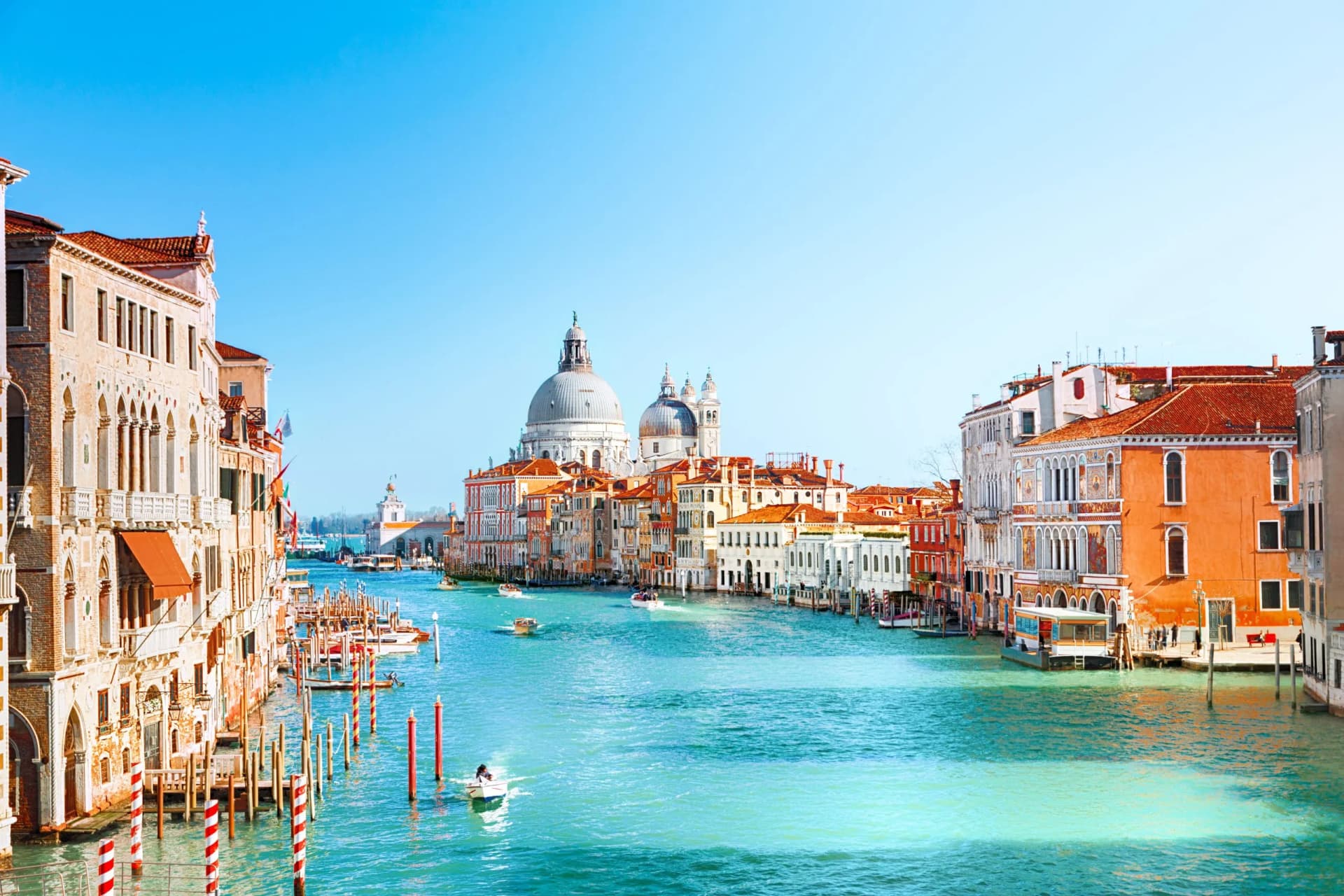 Boats on the Grand Canal in Venice with Santa Maria della Salute dome under clear blue sky.