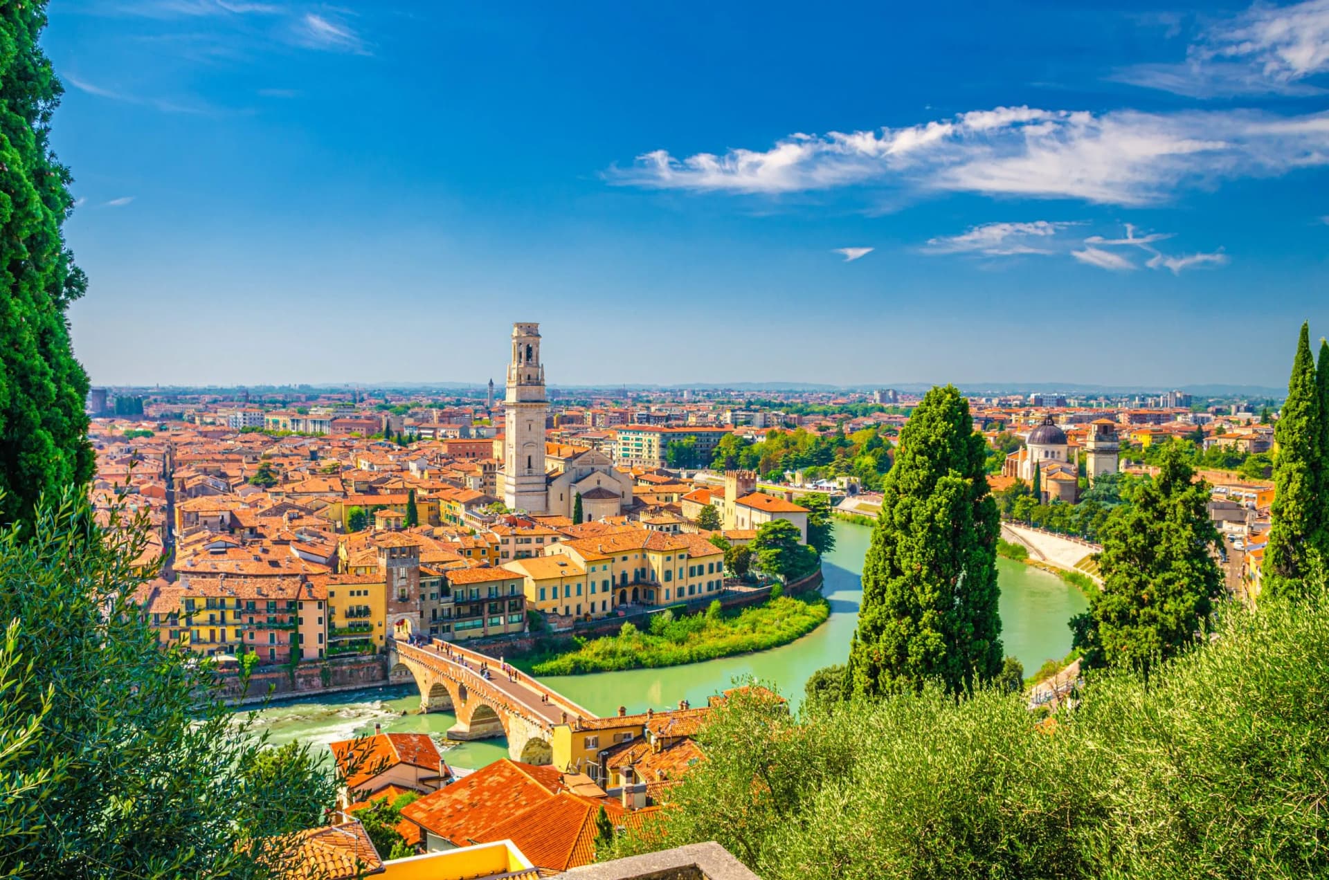 Verona cityscape with terracotta roofs, Ponte Pietra bridge, and Adige River under blue sky.