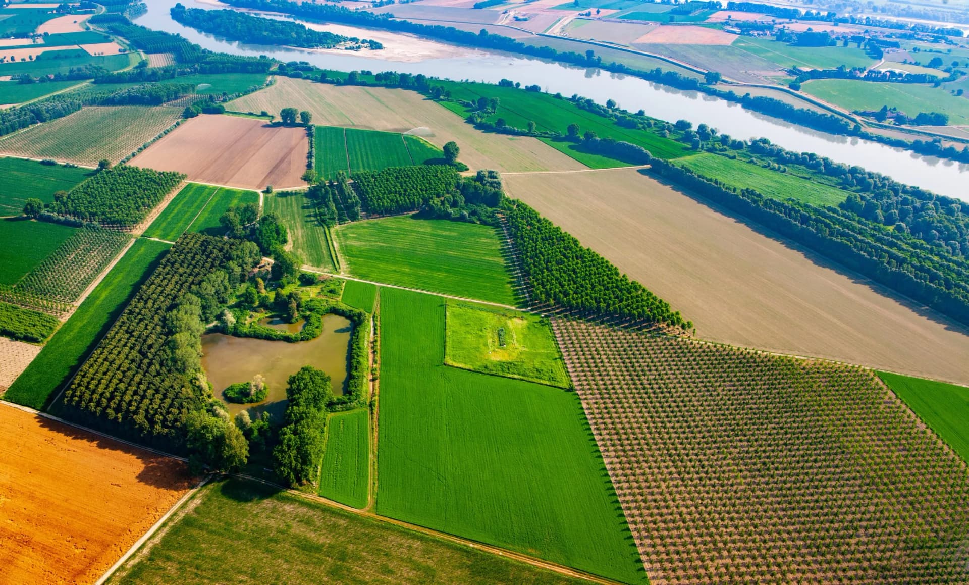 Aerial view of patchwork farmland, small pond, and river in the Po Valley region.