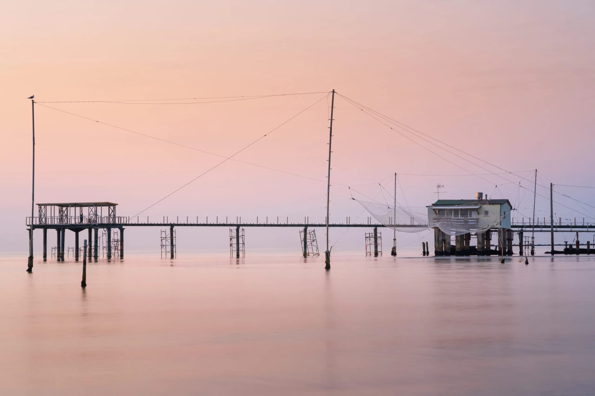 Fishing huts on stilts with nets over calm water at sunrise or sunset in Venice.
