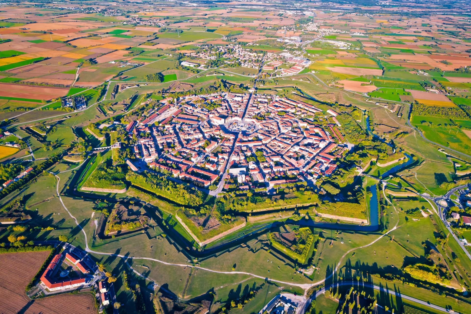 Aerial view of Palmanova, a star-shaped fortified city surrounded by green ramparts and farmland.