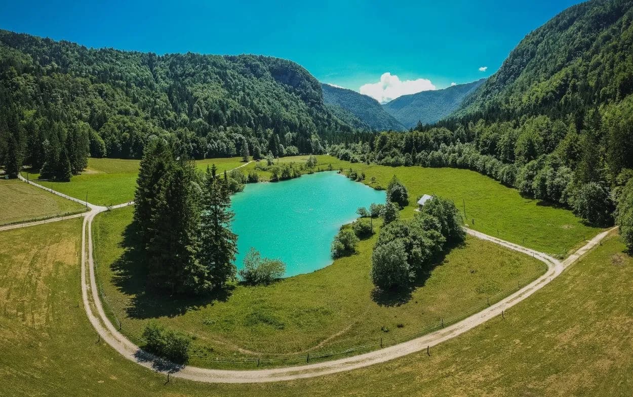 Turquoise alpine lake in Radovna Valley surrounded by green forested mountains under a blue sky.