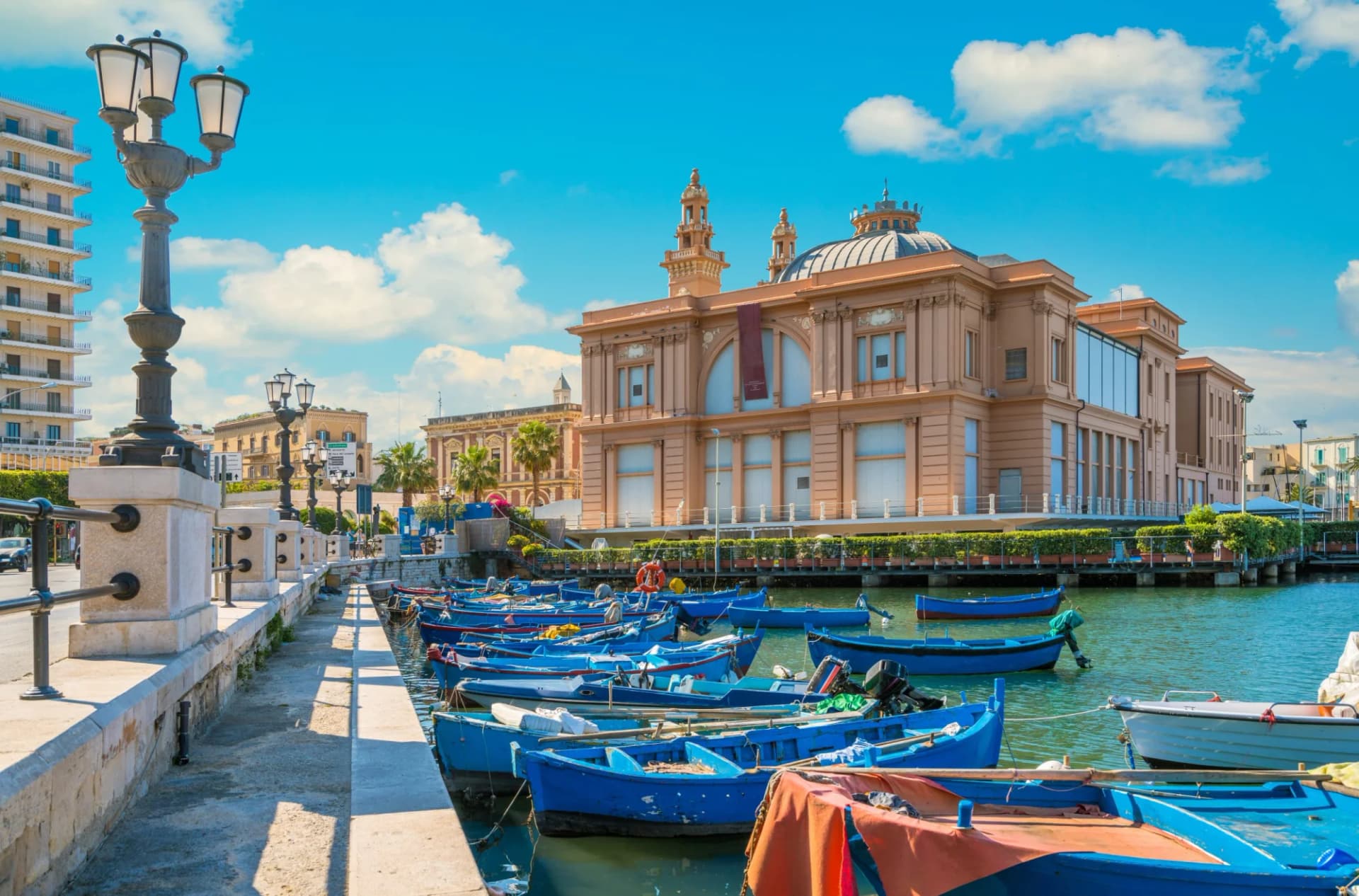 Blue fishing boats docked in harbor next to historic building in Bari, Italy.