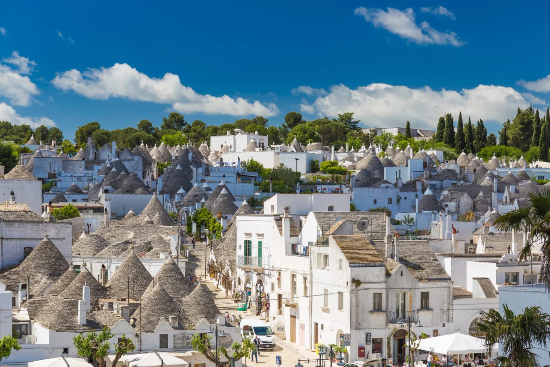 Alberobello trulli houses with conical stone roofs under a bright blue sky.