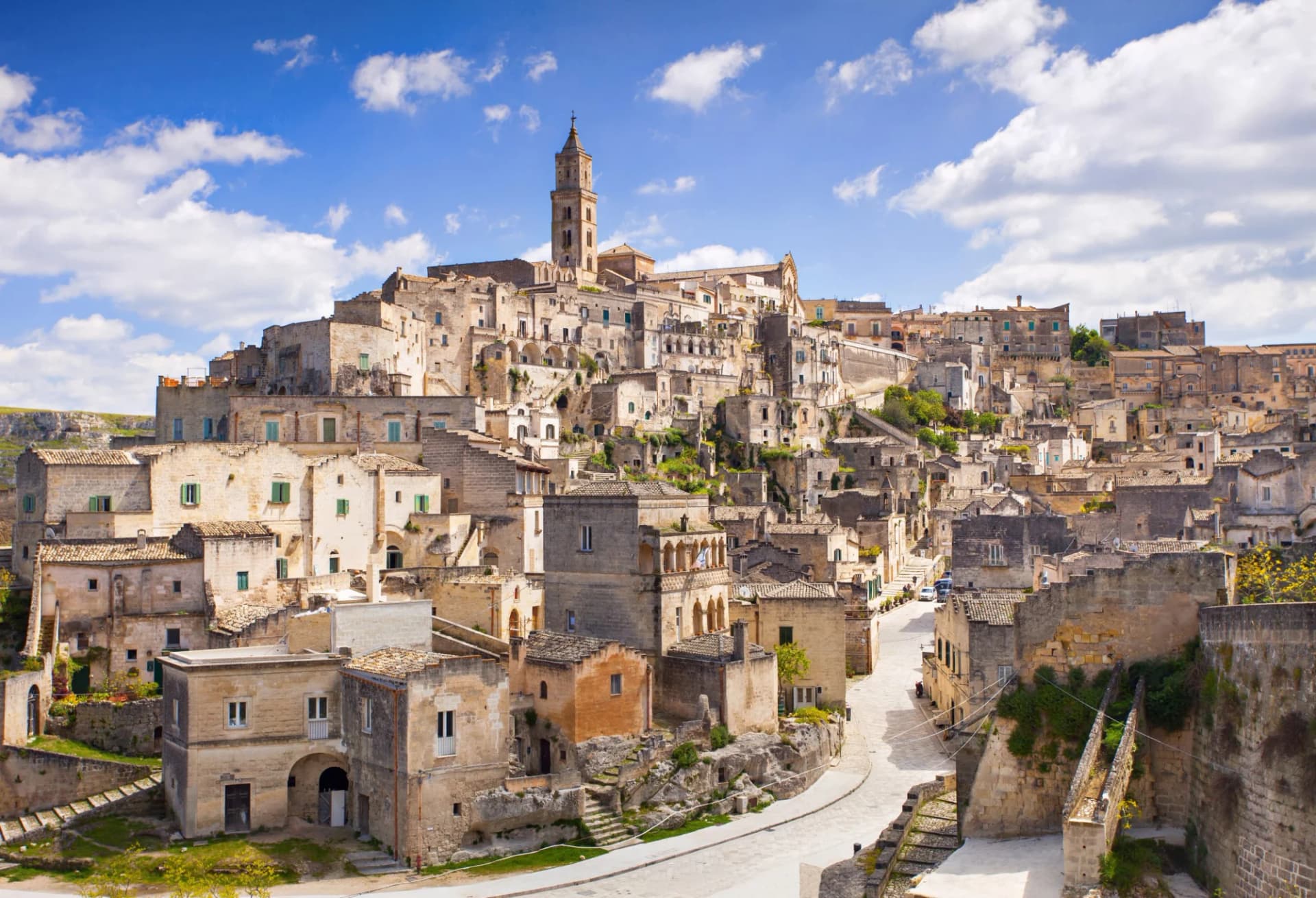 Historic stone city built into hillside with bell tower under blue sky, Matera.