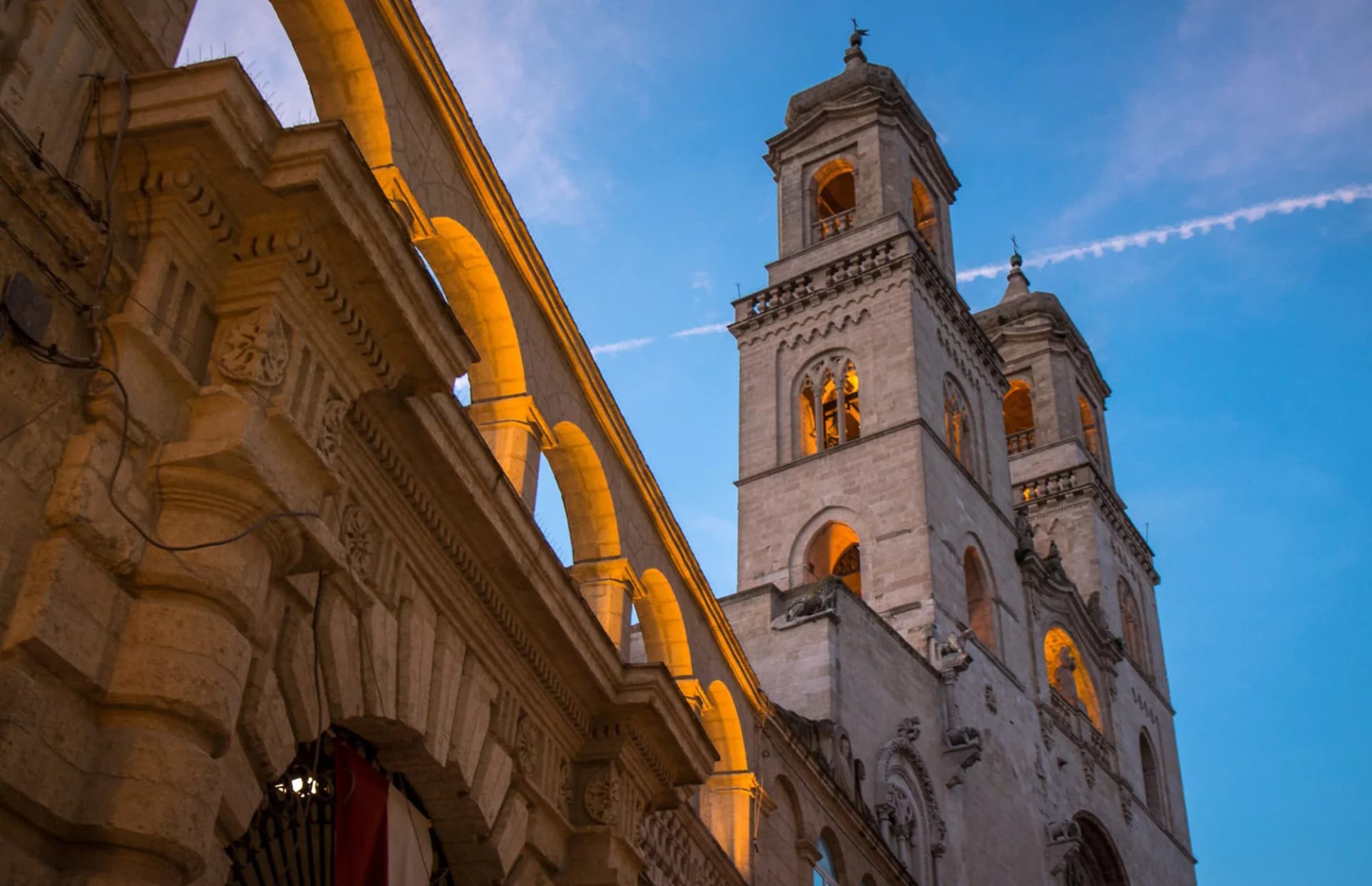 Stone cathedral towers illuminated against a blue twilight sky with an arched walkway.
