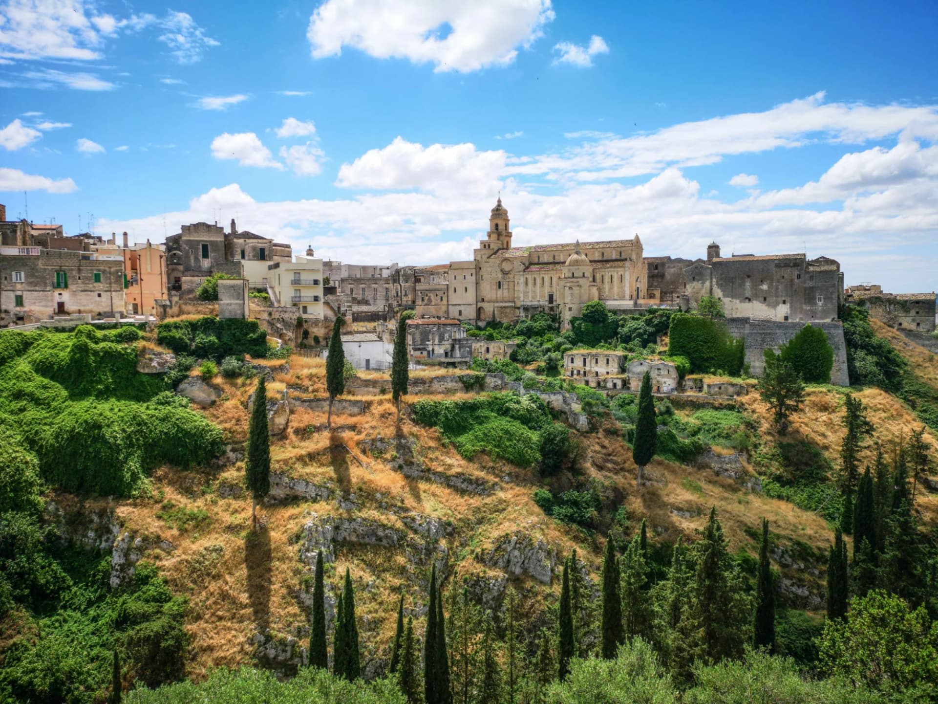 Historic town with a large cathedral atop a dry, green hillside under a blue sky in Altamura.