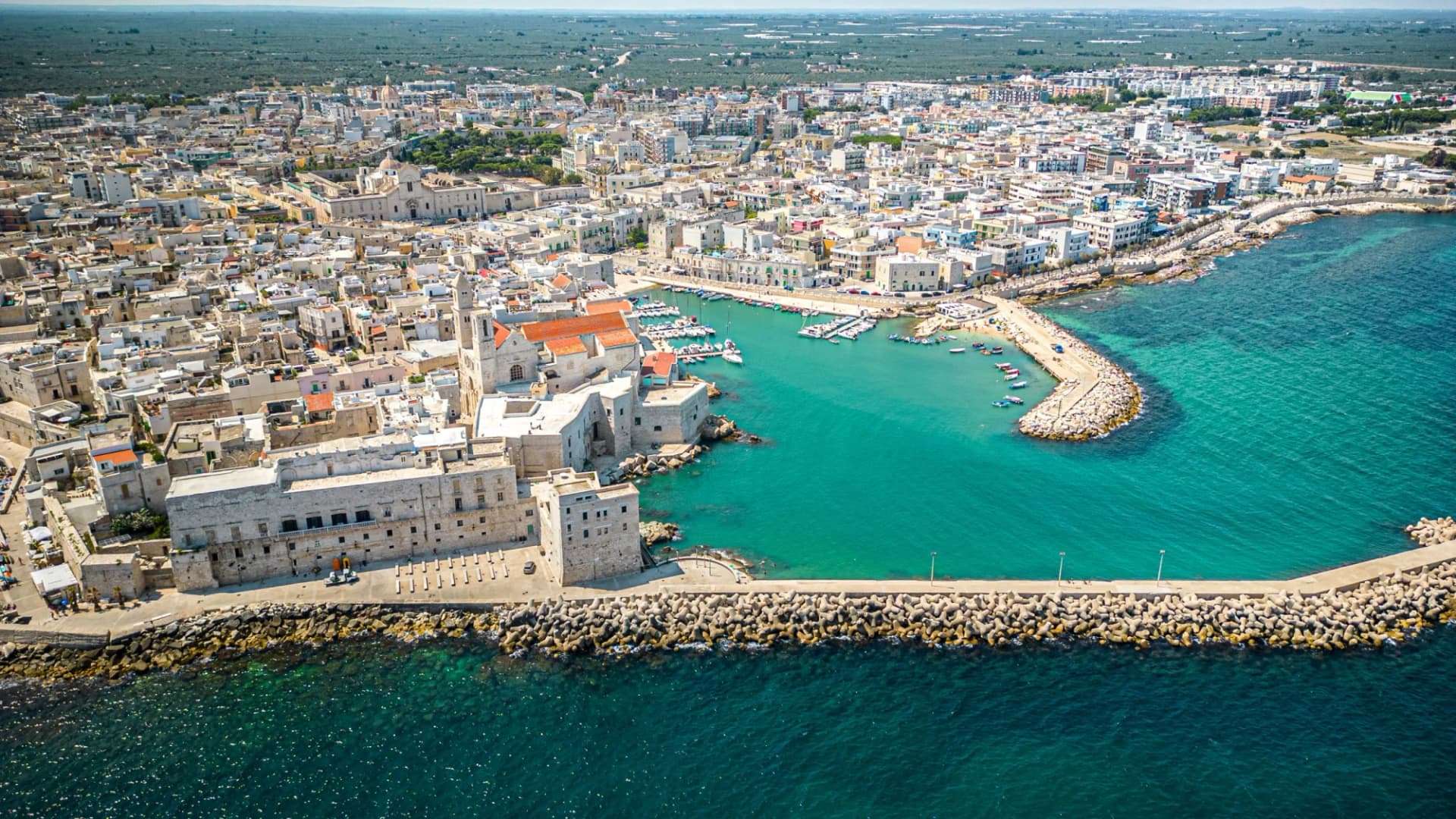 Aerial view of Giovinazzo coastal town with harbor, stone buildings, and turquoise Mediterranean sea.
