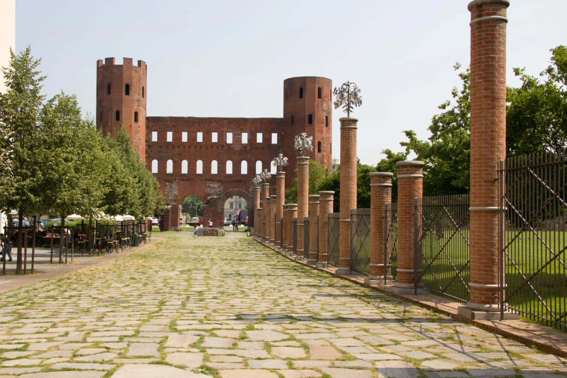 Porta Palatina in Torino with cobblestone path, brick columns, and outdoor cafe seating.