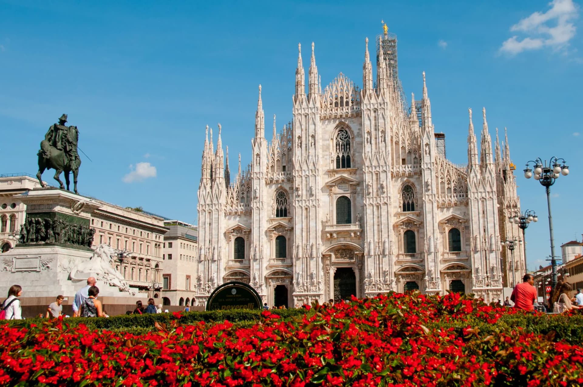 Milan Cathedral (Duomo) facade with red flowers and equestrian statue in foreground.