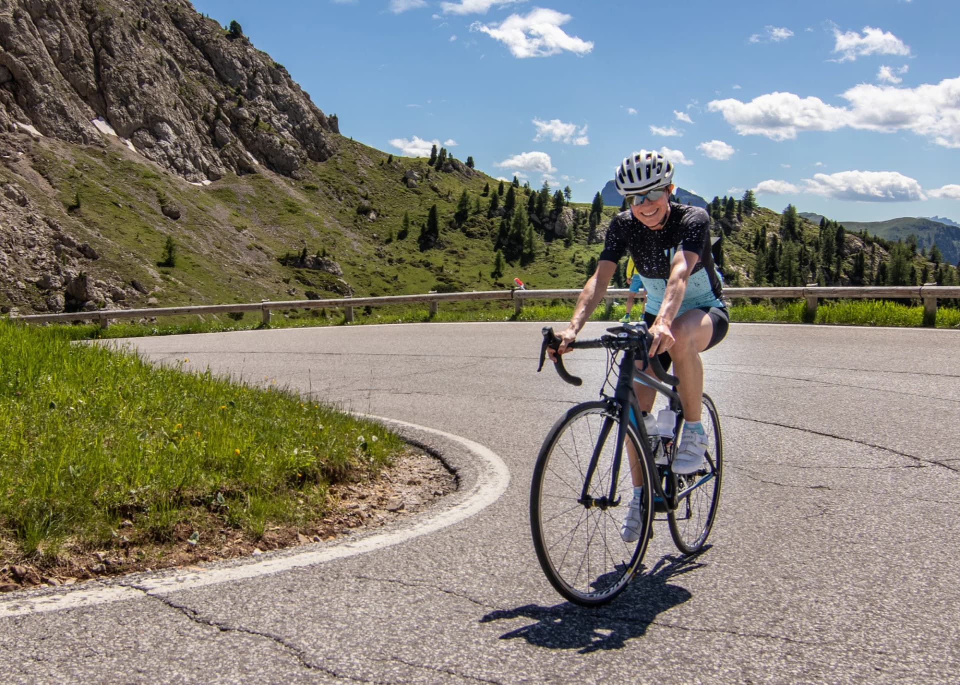 Cyclist riding a road bike on a mountain road with green slopes and blue sky