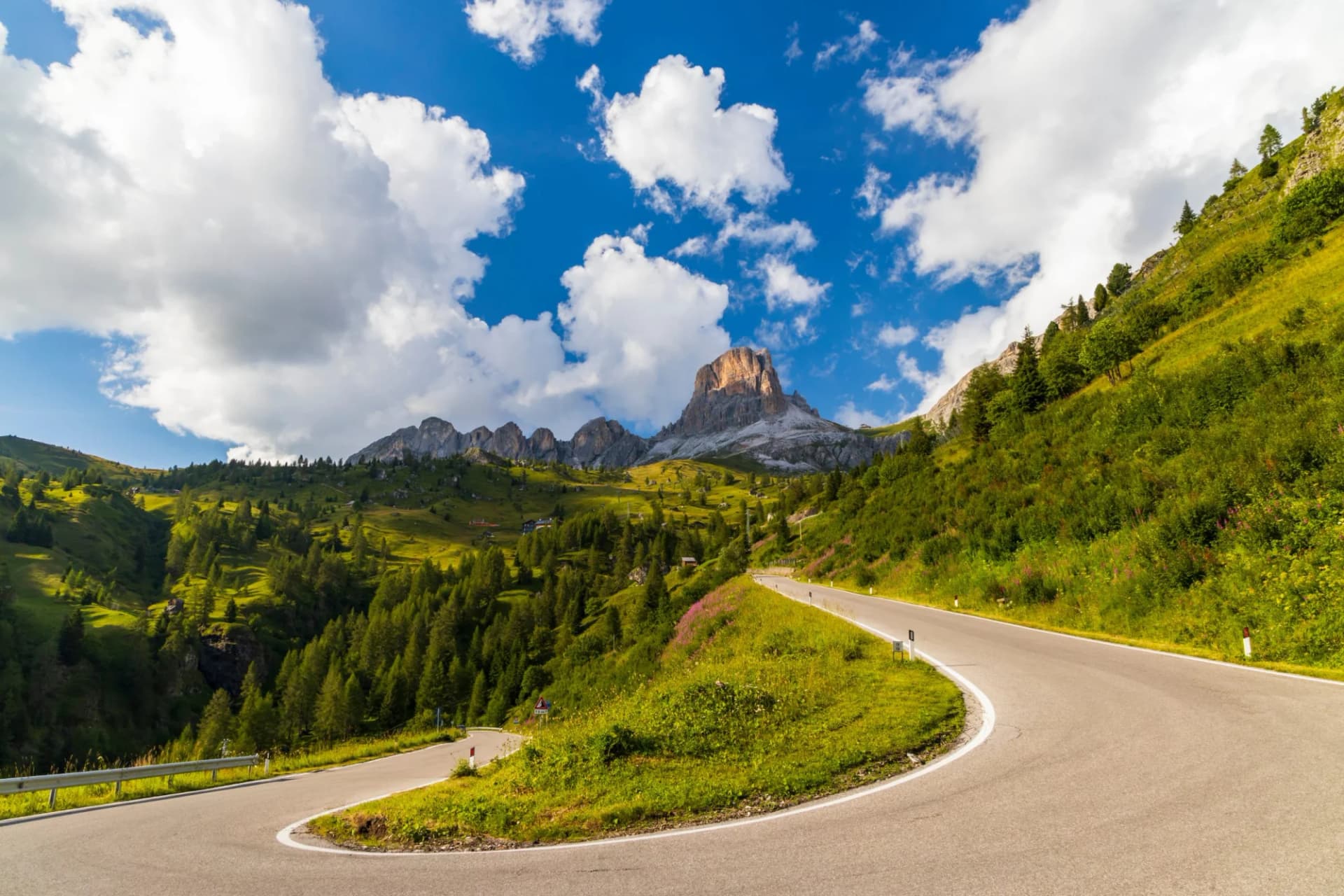 Winding mountain road near Passo Giau in Dolomites, Italy, with green slopes and rocky peaks.
