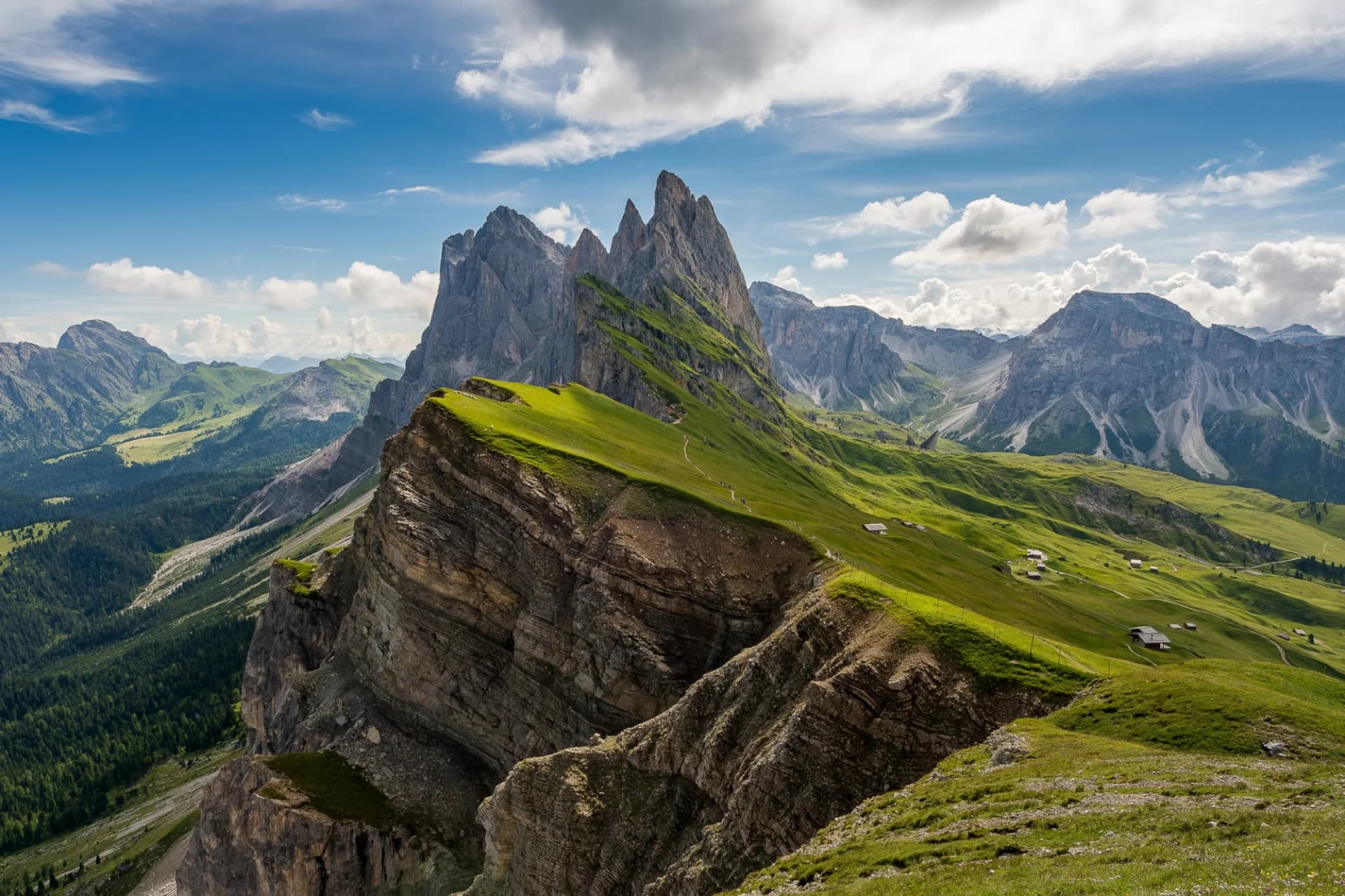 Sharp mountain peaks above green alpine meadows and steep rocky cliffs in the Dolomites.