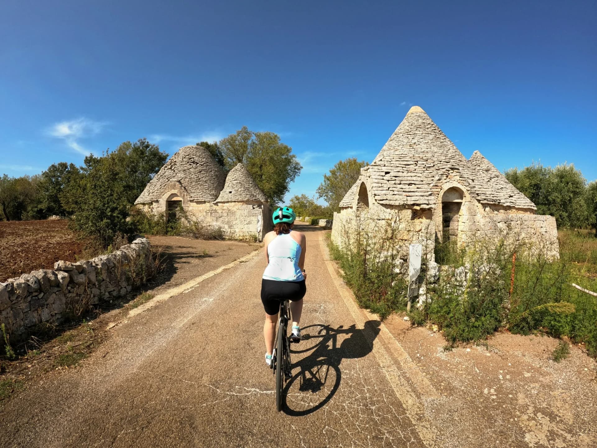 Cyclist riding past trulli stone huts on a sunny road in Puglia, Italy