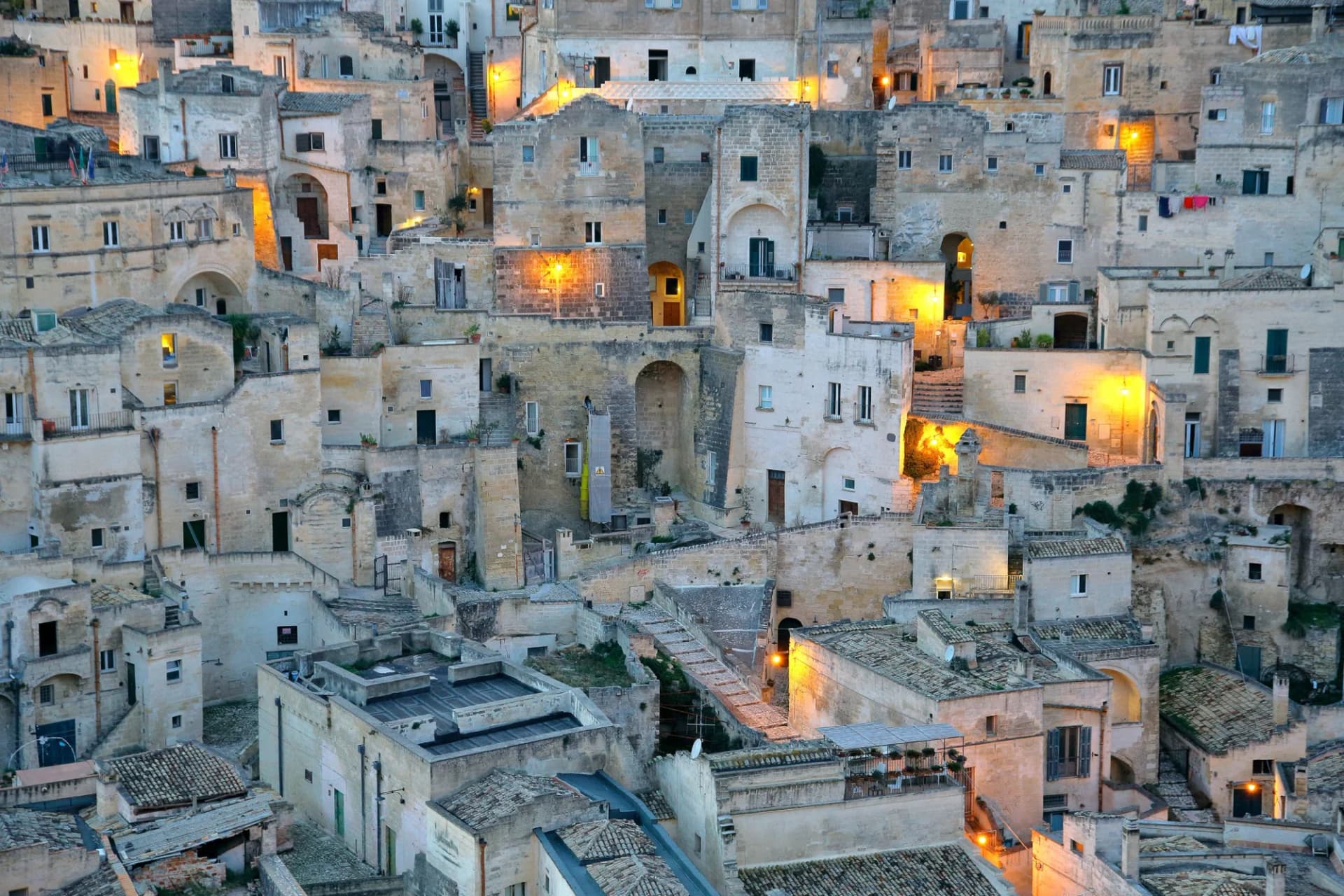 Stacked stone buildings illuminated at dusk in Matera, Italy.