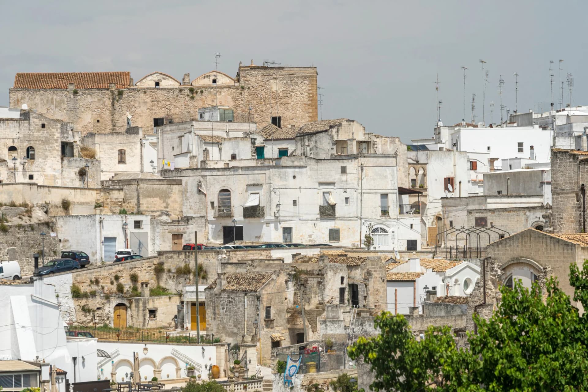 Historic town in Apulia with stacked white and stone buildings climbing a hillside under a gray sky.