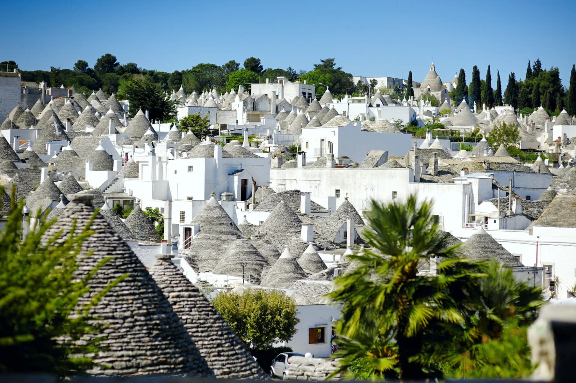 Trulli houses with conical stone roofs in Alberobello, Apulia, Italy, under a clear blue sky.