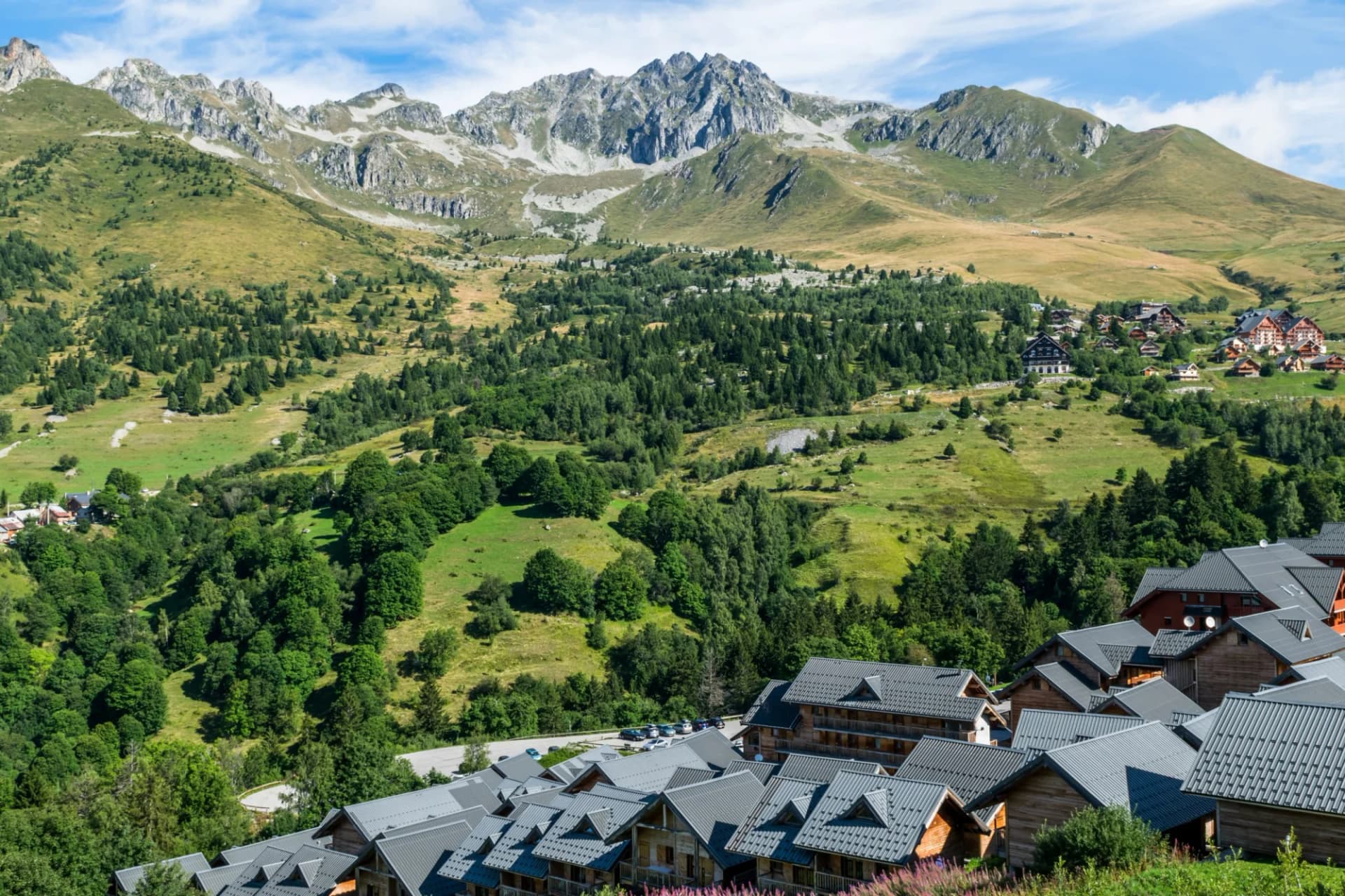 Alpine village with wooden chalets nestled in green mountainside below rocky peaks, Col de la Madeleine.