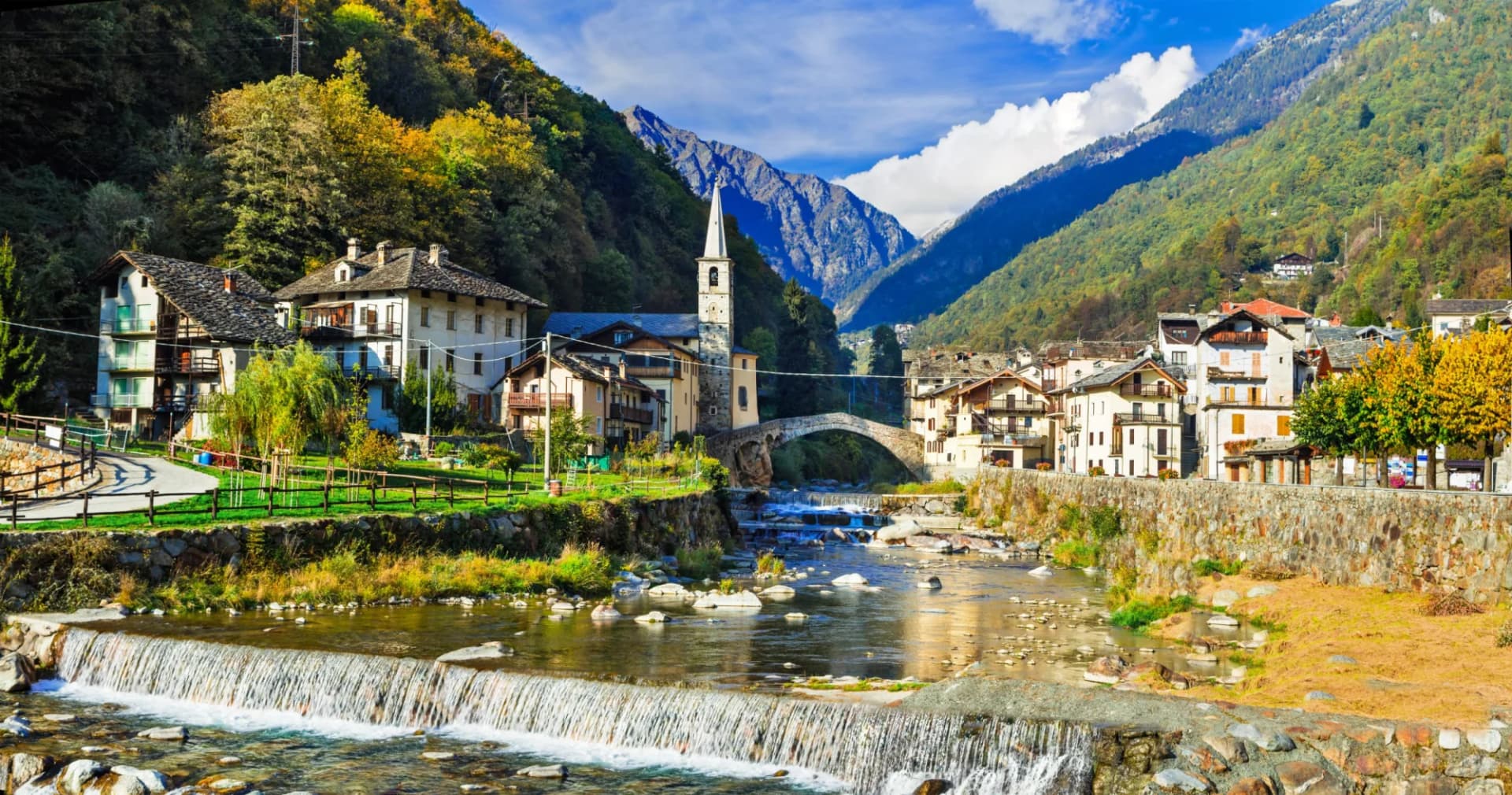 Alpine village with stone church and bridge over river, Valle d'Aosta mountains.