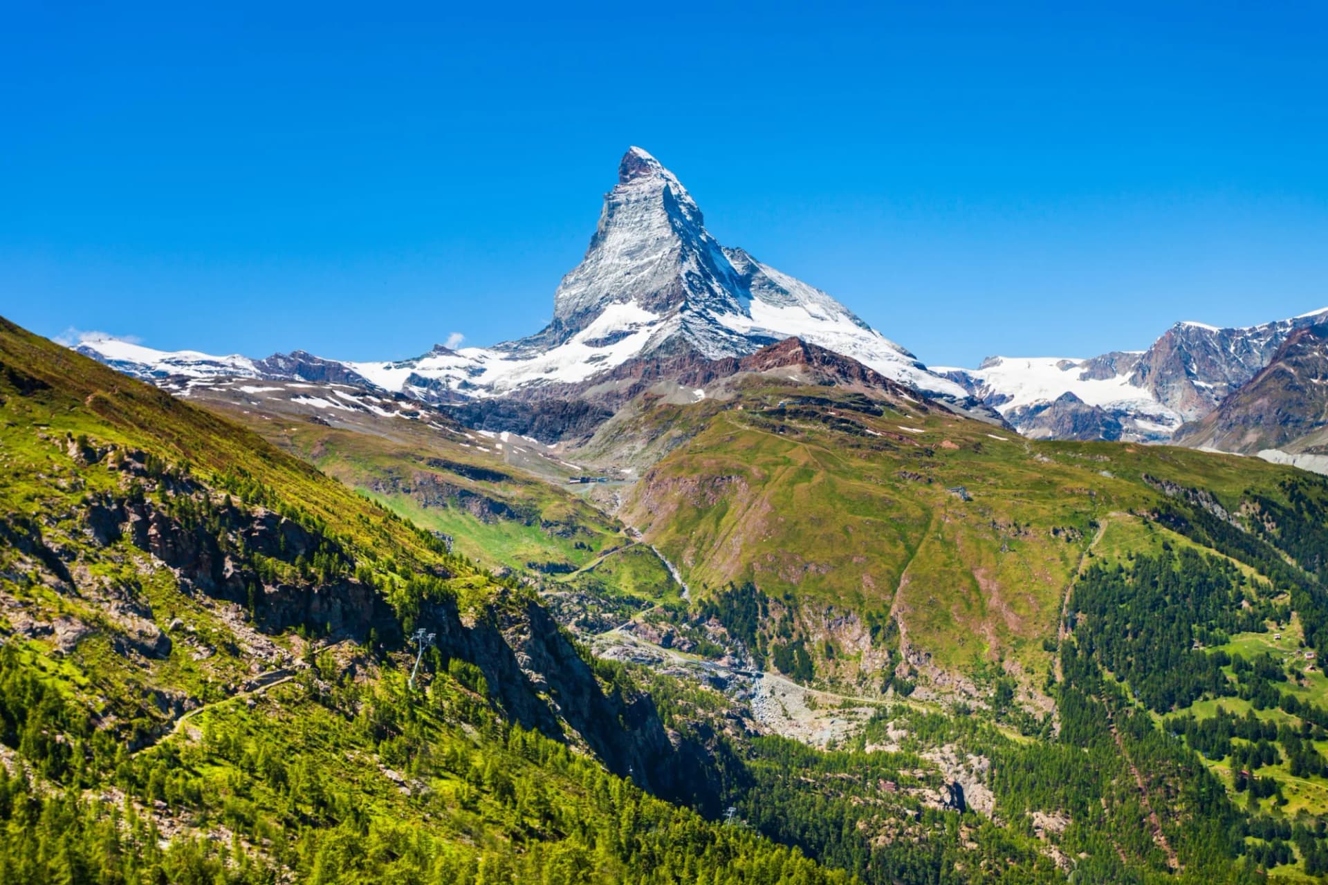 Matterhorn mountain range in Switzerland with snow-capped peaks and green summer slopes under blue sky.