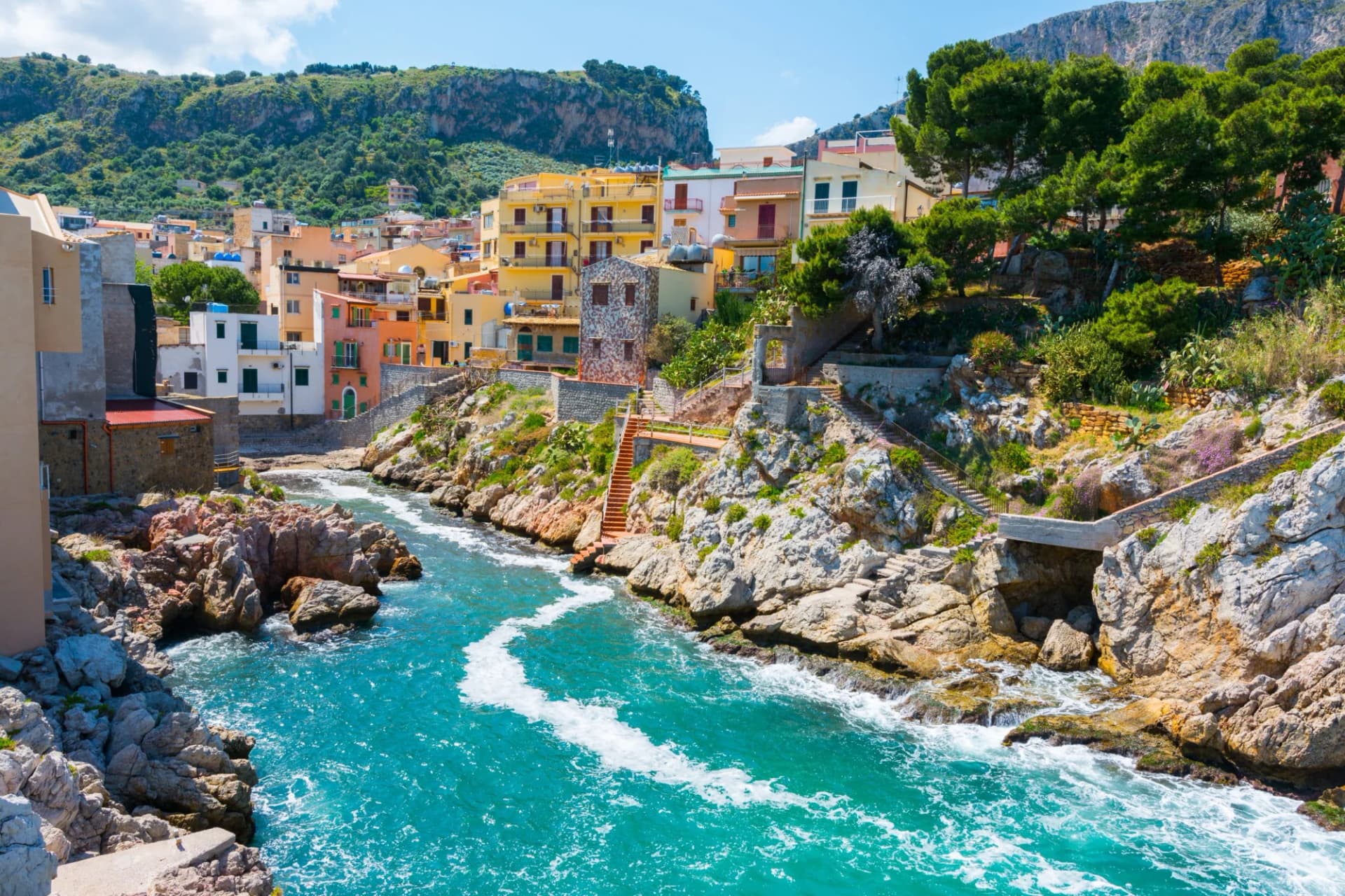 Colorful coastal town built into rocky cliffs above turquoise Mediterranean water in Santa Flavia, Sicily.