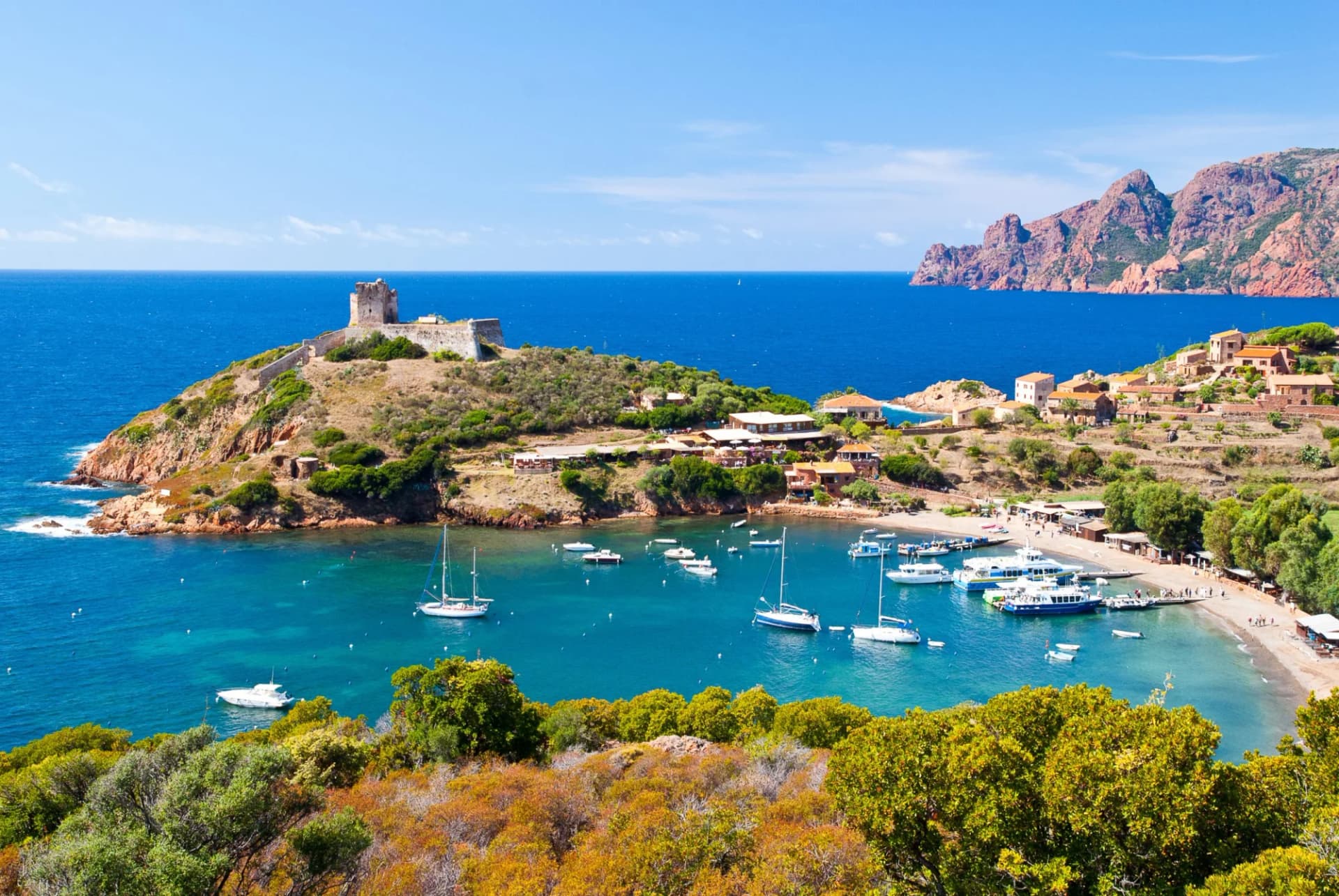 Boats anchored in turquoise bay below historic tower on rocky peninsula, Girolata.