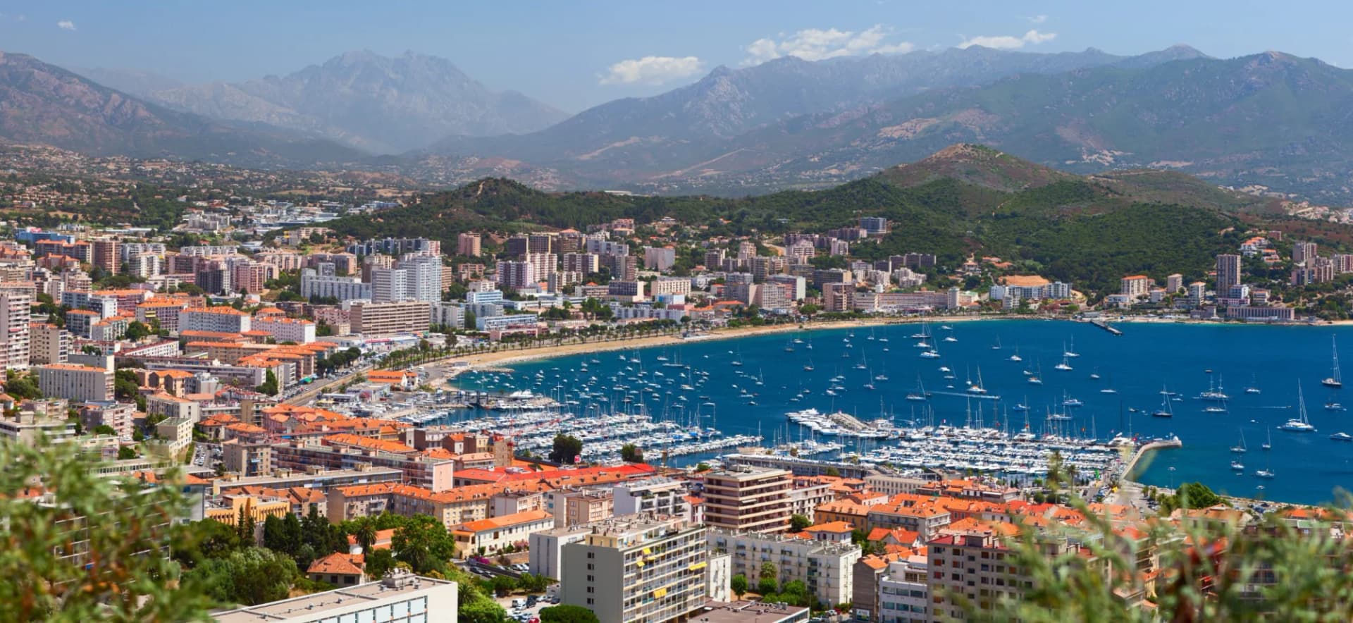 Aerial view of Ajaccio town, harbor full of sailboats, and mountains in the background.