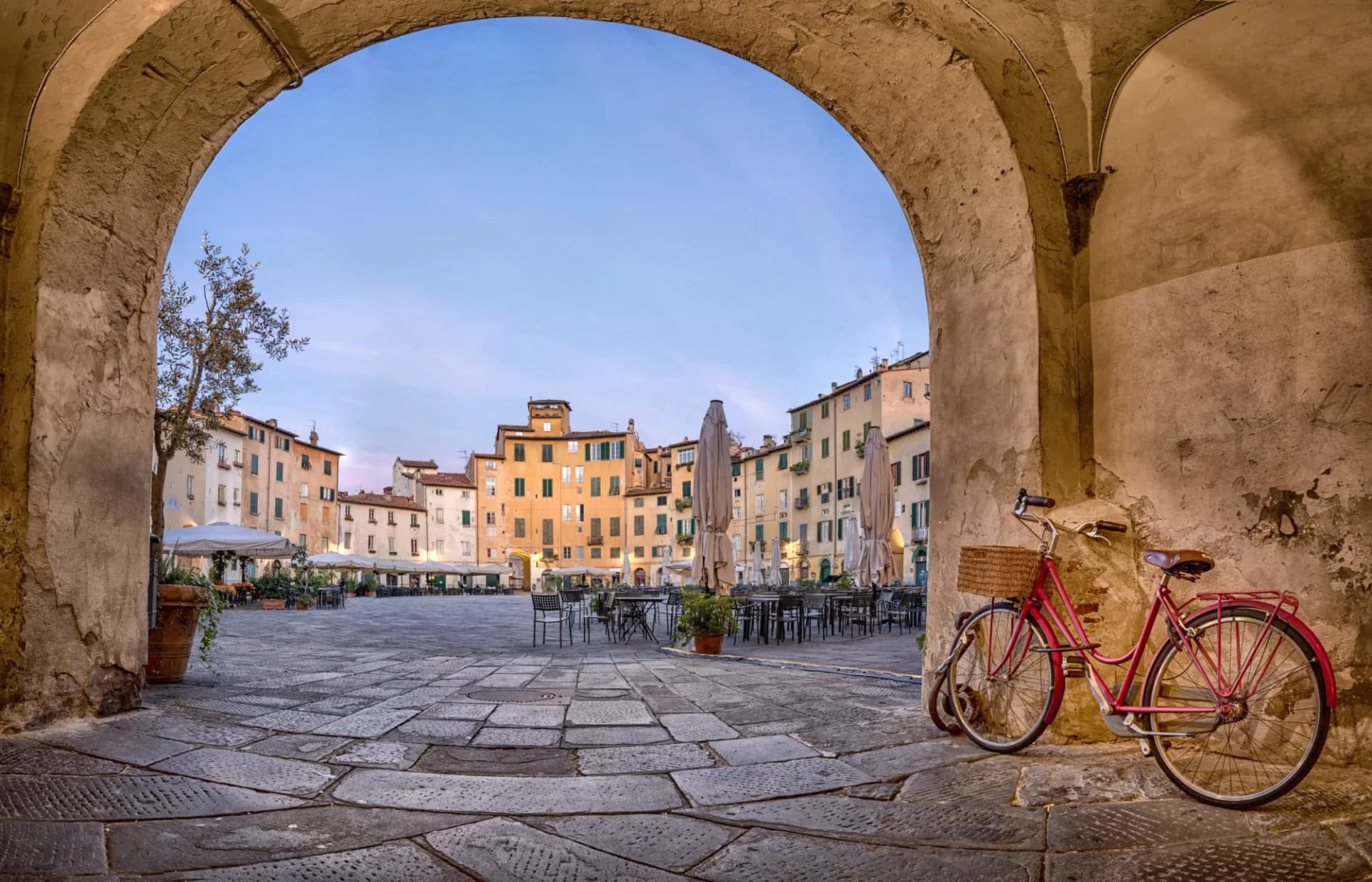 Red bicycle parked under archway overlooking Lucca's Piazza dell'Anfiteatro, Italy.