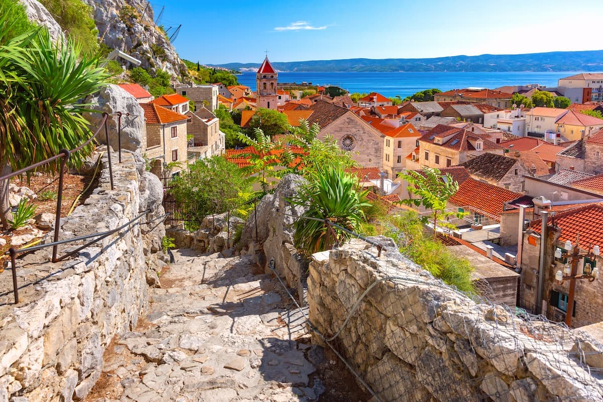 Stone steps descending past coastal town with red roofs and blue sea view