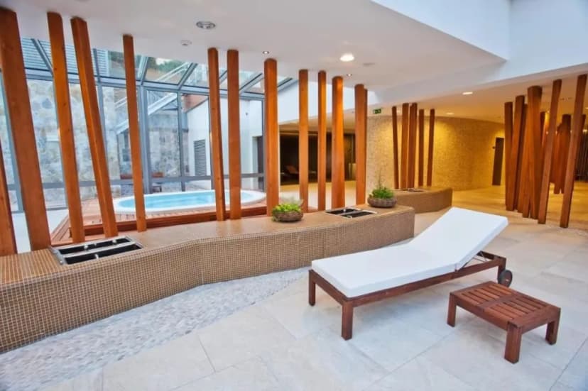 Indoor spa relaxation area with lounge chair, jacuzzi visible through glass, and wooden pillars.