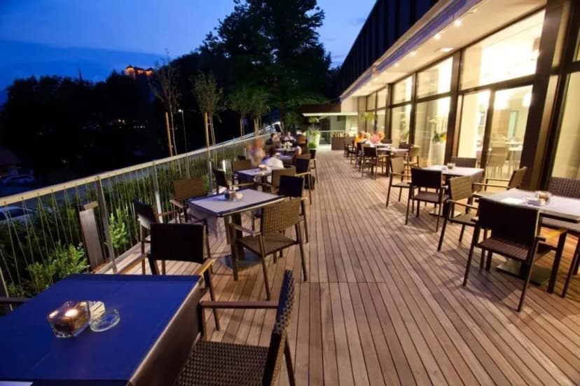 Hotel Astoria outdoor terrace dining area with wooden deck at dusk overlooking a dark, wooded hillside.