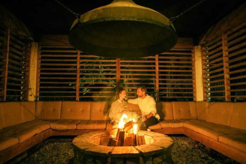 Couple relaxing by outdoor stone fire pit under large metal hood in Garden Village Bled.