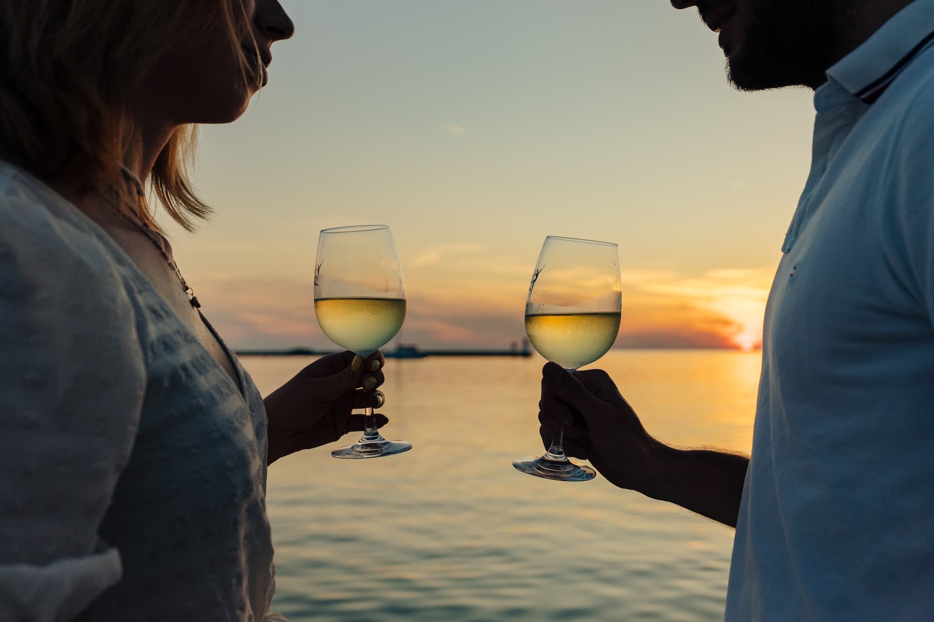 Couple toasting with white wine glasses on the Adriatic Sea at sunset
