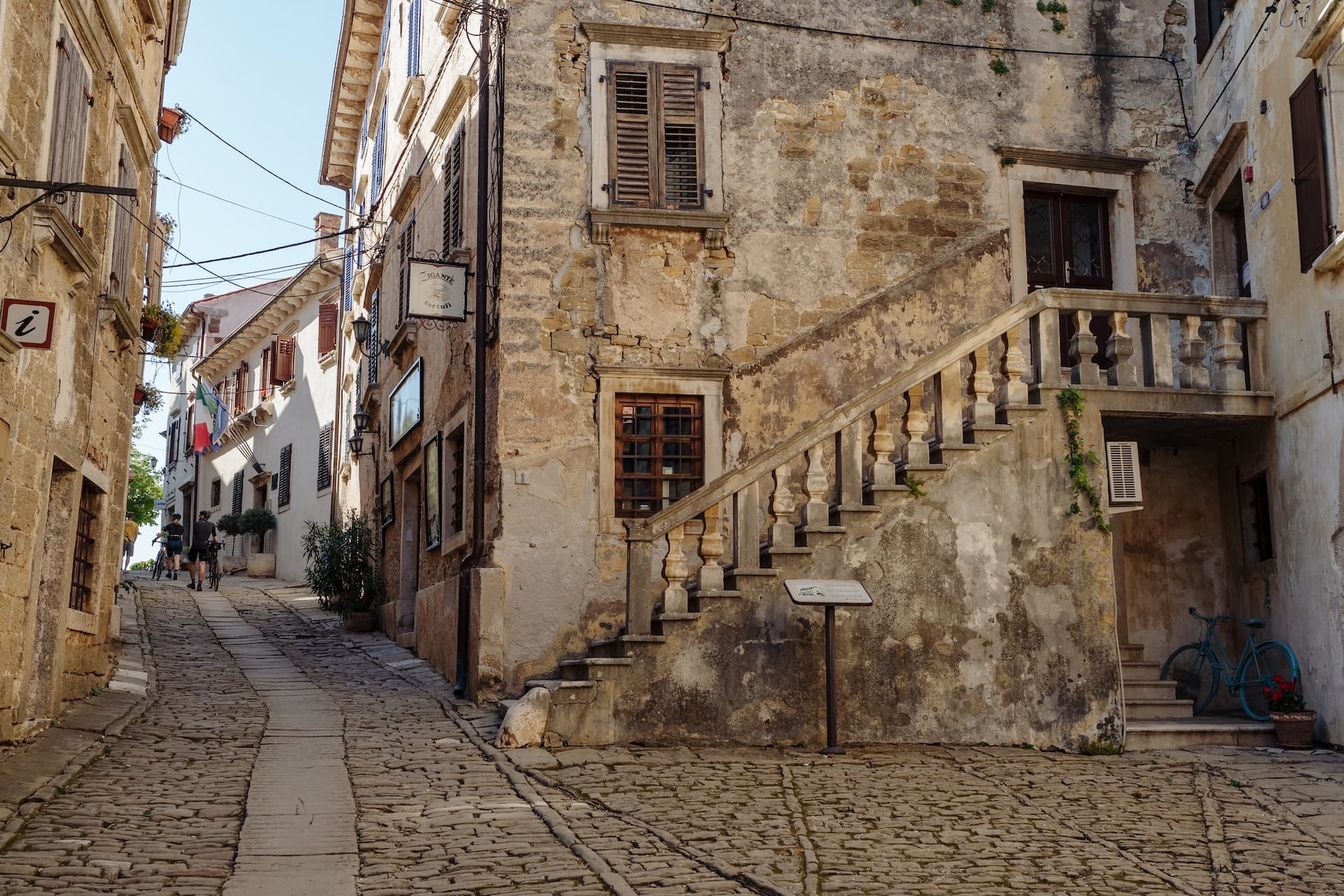 Cobblestone street uphill in Grožnjan with old stone buildings and a turquoise bicycle.