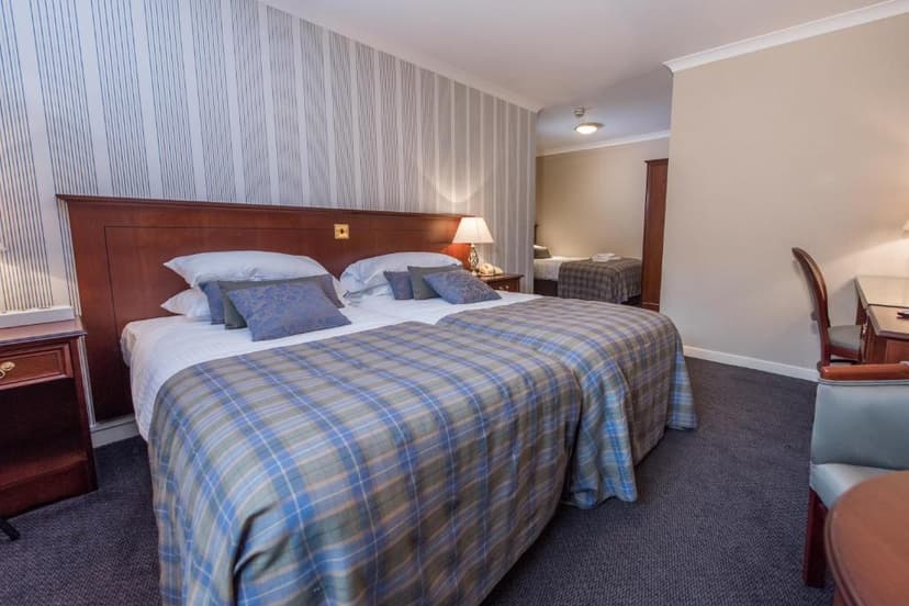 Twin beds with blue plaid blankets in a hotel room, view into an adjoining room.