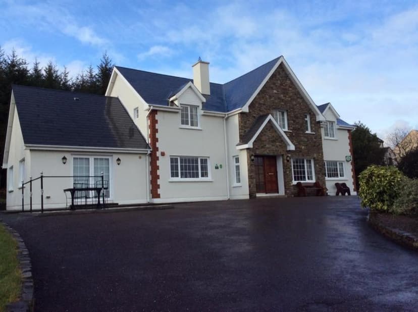 Sneem River Lodge with white walls, stone facade, and dark slate roof under blue sky.