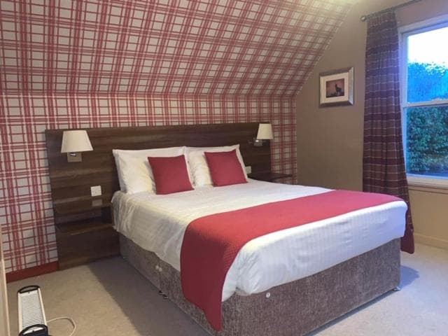 Hotel room with double bed, red plaid wallpaper, and window view of greenery