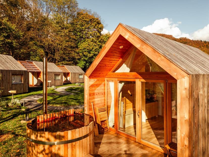 Wooden glamping cabin with outdoor hot tub, surrounded by autumn trees and hills